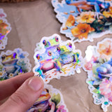 Pastel Frogs Holographic Handmade Sticker Set of 8, natural flower elements and cute style. Dive into a world of whimsy with our handcrafted "Pastel Frogs" sticker set. Each of the 8 stickers is a testament to originality, handcrafted on high-quality adhesive paper with a delightful holographic effect.