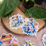 Pastel Frogs Holographic Handmade Sticker Set of 8, natural flower elements and cute style. Dive into a world of whimsy with our handcrafted "Pastel Frogs" sticker set. Each of the 8 stickers is a testament to originality, handcrafted on high-quality adhesive paper with a delightful holographic effect.