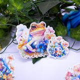 Pastel Frogs Holographic Handmade Sticker Set of 8, natural flower elements and cute style. Dive into a world of whimsy with our handcrafted "Pastel Frogs" sticker set. Each of the 8 stickers is a testament to originality, handcrafted on high-quality adhesive paper with a delightful holographic effect.